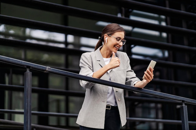 Une femme d'affaires heureuse s'appuie sur la balustrade tout en ayant un appel vidéo sur son téléphone