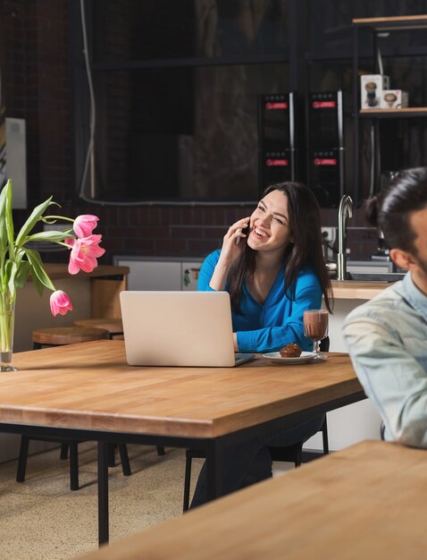 Femme d'affaires heureuse travaillant sur ordinateur portable, parlant sur smartphone et buvant du café dans un café. Concept d'espace de vie, d'affaires, de loisirs, de co-working