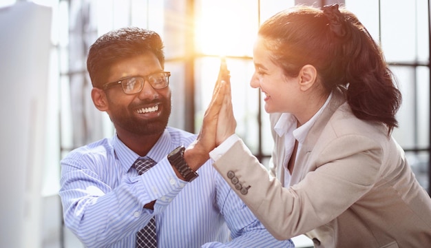 Femme d'affaires heureuse utilisant un ordinateur portable tout en travaillant avec un collègue au bureau high five