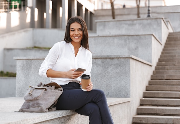 Femme d'affaires heureux assis à l'extérieur avec une tasse de café
