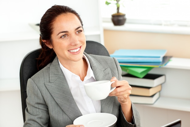 Femme d&#39;affaires hispanique joyeuse, boire du café à son bureau