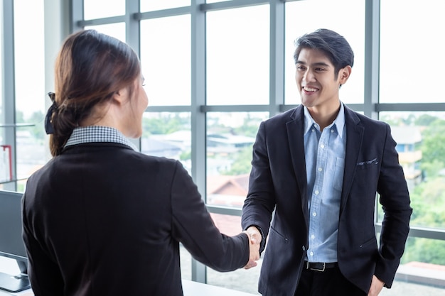 Femme d'affaires et homme d'affaires asiatiques se serrant la main à l'arrière-plan de la salle de bureau après la signature du contrat ou l'accord de salutation de la poignée de main, l'entreprise a exprimé sa confiance enhardie et en couple réussi