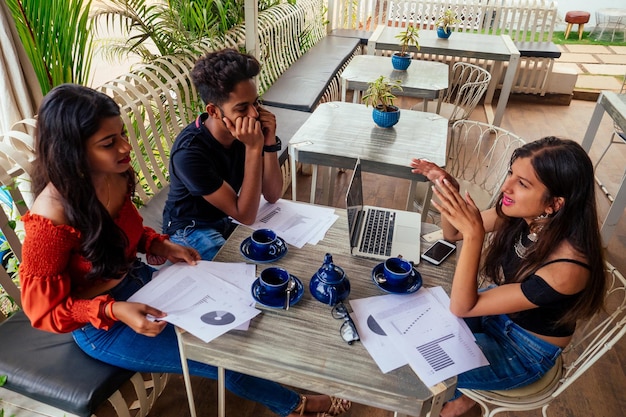 Femme d'affaires et homme d'affaires indiens prospères au travail surfant en freelance en ligne indépendante dans un café tropical d'été.trois amis communiquant avec du thé se rencontrant