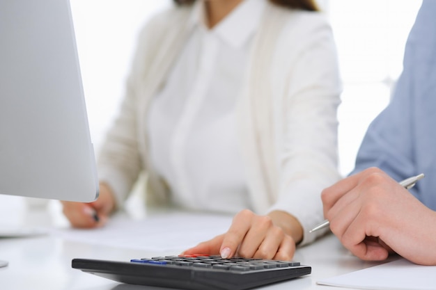 Femme d'affaires et homme assis et travaillant avec un ordinateur et une calculatrice au bureau