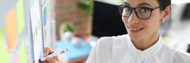 Femme d'affaires intelligente dans des verres tenir le marqueur bleu contre le tableau blanc. Concept d'éducation commerciale