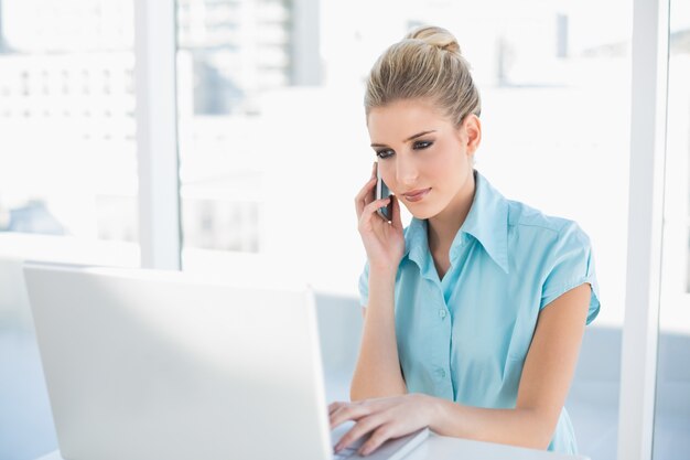 Femme d&#39;affaires intelligente détendue au téléphone tout en utilisant un ordinateur portable