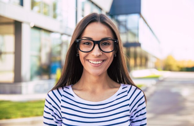 Une femme d'affaires intelligente portant une tenue décontractée et des lunettes pose les bras croisés, regardant vers la gauche et souriant sincèrement