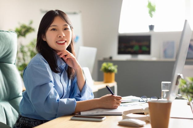 Femme d'affaires japonaise à l'aide d'un ordinateur travaillant en ligne posant assis au bureau