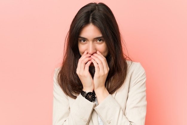 Femme d'affaires jeune brune contre une rose en riant de quelque chose, couvrant la bouche avec les mains.