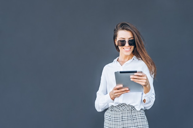 Femme d'affaires jeune avec café et tablette sur fond gris.