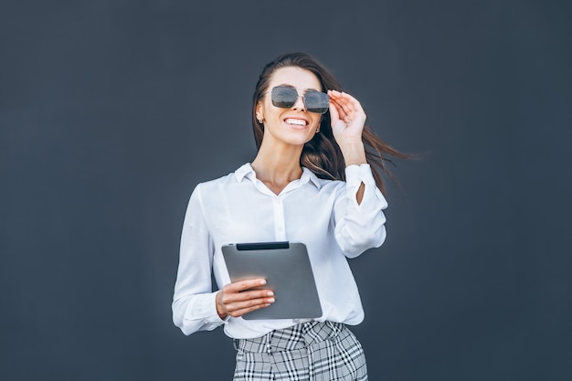 Femme d'affaires jeune avec café et tablette sur fond gris.