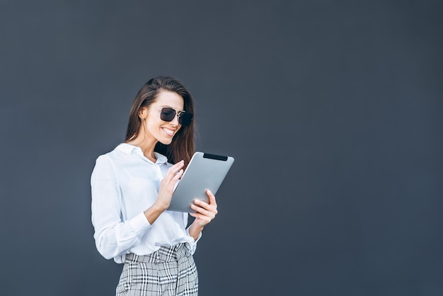 Femme d'affaires jeune avec café et tablette sur fond gris.