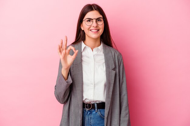 Femme d'affaires jeune caucasien sur rose gai et confiant montrant le geste ok.