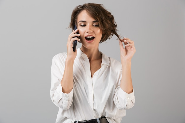 Femme d'affaires jeune émotionnelle posant isolé sur mur gris parler par téléphone mobile