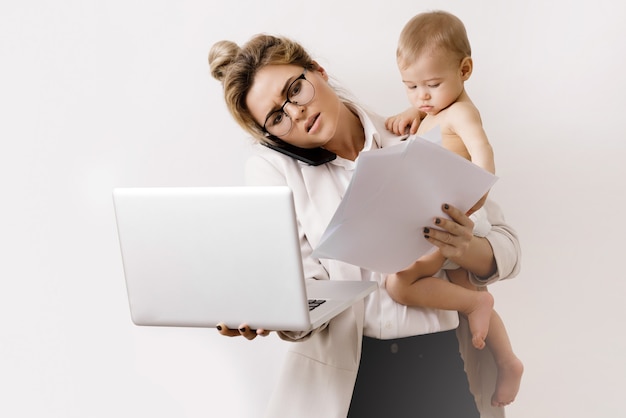 Une femme d'affaires jeune et occupée travaille et tient son petit bébé. Concepts d'échelle de carrière ou de congé de maternité.