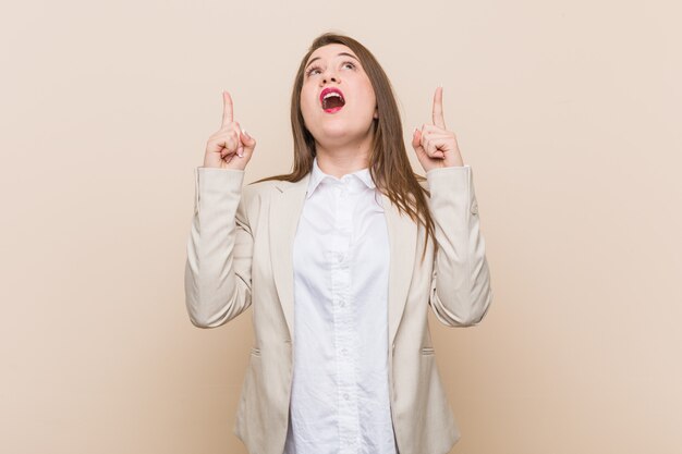 Femme d'affaires jeune pointant à l'envers avec la bouche ouverte.