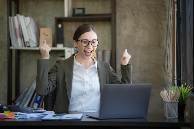 Une femme d'affaires joyeuse célèbre sa réalisation en lisant de bonnes nouvelles sur un ordinateur portable du bureau.