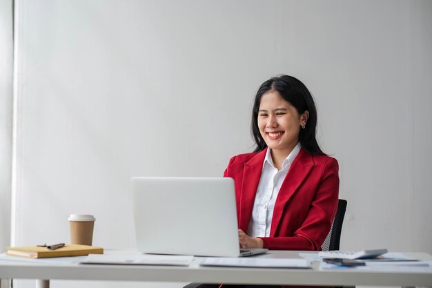 Photo une femme d'affaires joyeuse travaillant sur un ordinateur portable au bureau asiatique heureuse belle femme d'affaires en costume officiel travaille sur le lieu de travail femme employée attrayante sourire de travailleuse de bureau