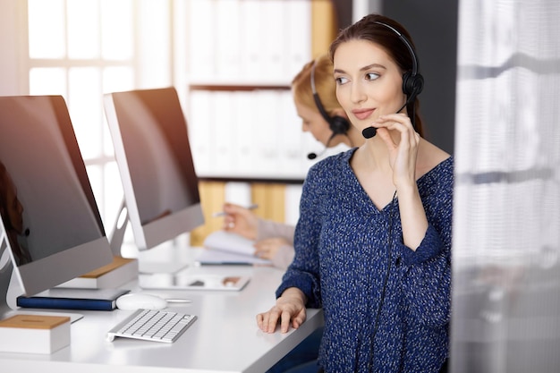 Femme d'affaires latino-américaine parlant par casque alors qu'elle était assise dans un bureau ensoleillé. Centre d'appels et groupe de personnes diverses dans les affaires.