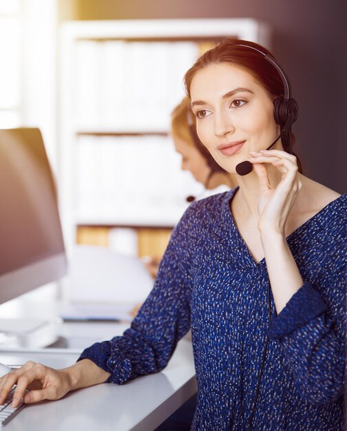 Femme d'affaires latino-américaine parlant par casque dans un bureau ensoleillé. Centre d'appels et groupe de personnes diverses dans les affaires.