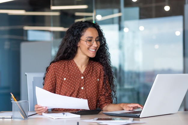 Femme d'affaires latino-américaine travaillant à l'intérieur du bureau avec des documents et des documents de travail d'ordinateur portable