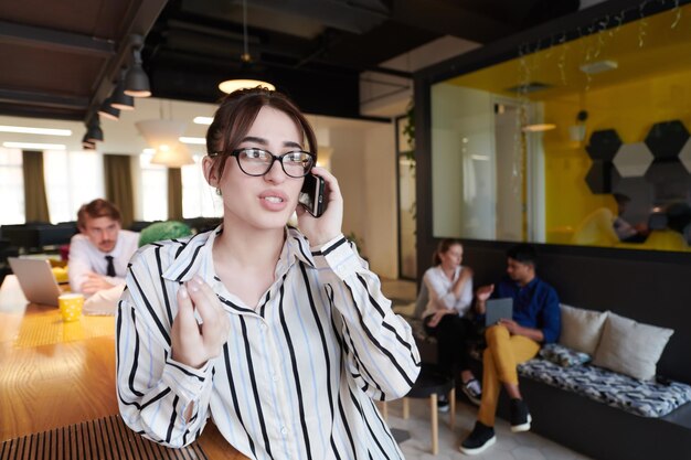 femme d'affaires avec des lunettes à l'aide d'un téléphone portable à l'intérieur d'un bureau à plan ouvert de démarrage moderne