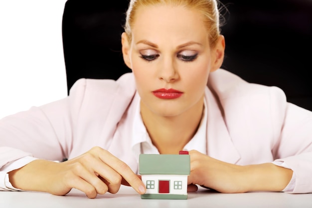 Une femme d'affaires avec une maison modèle assise sur un fond blanc