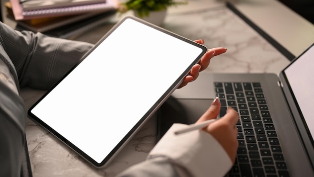 Une femme d'affaires avec une maquette d'écran blanc de tablette numérique et un ordinateur portable sur son bureau