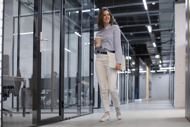 Femme d'affaires marchant le long du couloir du bureau avec des documents.