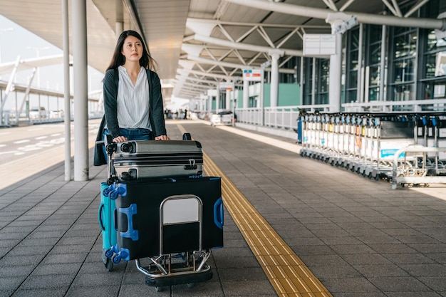 femme d'affaires marchant rapidement à travers le chariot à bagages et la voiture roulante. jeune femme allant travailler à l'étranger en visitant des clients. femme élégante à l'extérieur de l'aéroport international avec chariot en journée ensoleillée.