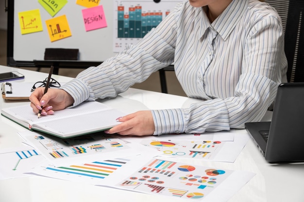 Femme d'affaires marketing en blazer gris au bureau avec ordinateur en gros plan en prenant des notes