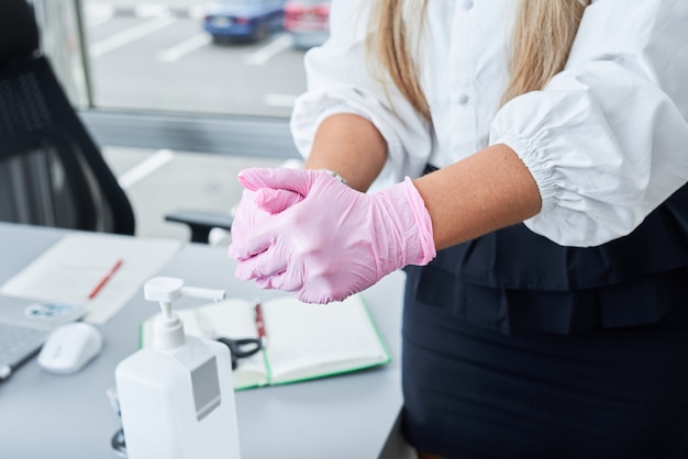 Femme d'affaires avec masque facial et gants à l'aide d'un désinfectant pour les mains au bureau. Protection contre le Corona virus.