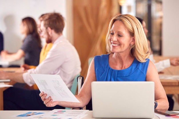 Femme d'affaires mature avec ordinateur portable travaillant sur table dans un café de bureau