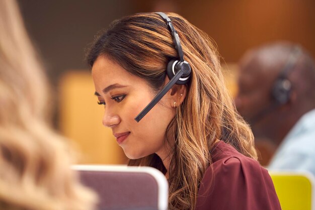 Femme d'affaires mature portant un casque téléphonique parlant à l'appelant dans un centre de services client occupé