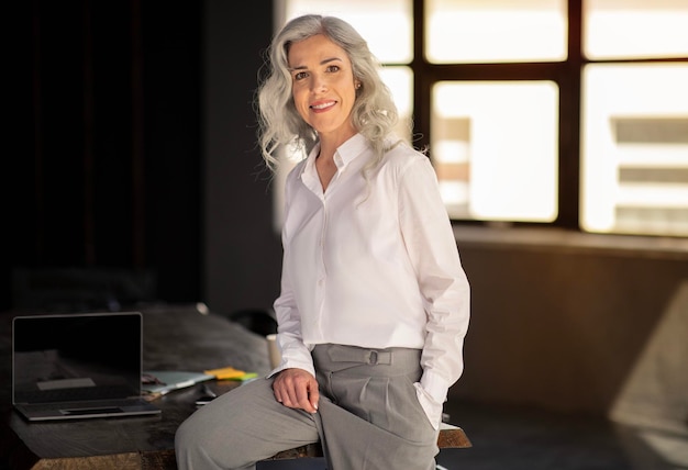 Femme d'affaires mature réussie assise sur une table dans un bureau moderne