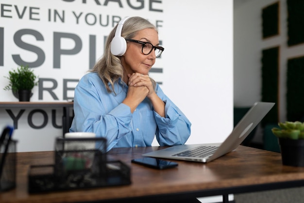 Photo femme d'affaires mature sérieuse regardant un webinaire sur un ordinateur portable au bureau avec ses mains