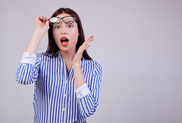 Femme d'affaires mignon aux cheveux bruns, lèvres roses pleines posant. Elle porte une chemise à rayures blanches et bleues et des lunettes d'ordinateur noires. surpris. regarde de côté. Copiez l'espace.