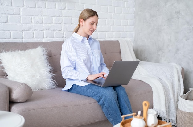 Femme d'affaires millénaire utilisant un ordinateur portable assis sur un canapé dans le salon