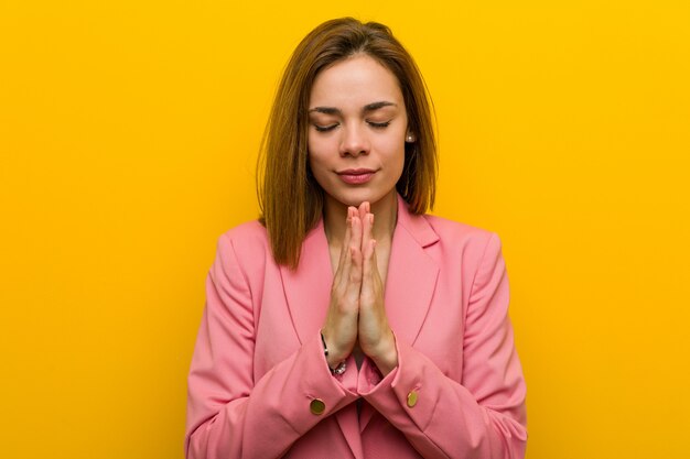 Femme d&#39;affaires de mode jeune tenant les mains dans la prière près de la bouche, se sent confiant.