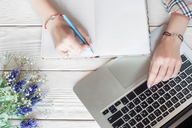 Femme d'affaires à la mode travaillant avec ordinateur portable. Vue de dessus sur les mains des étudiantes dans des bracelets cool, écrivant dans les produits laitiers et en tapant sur un ordinateur portable, mise à plat