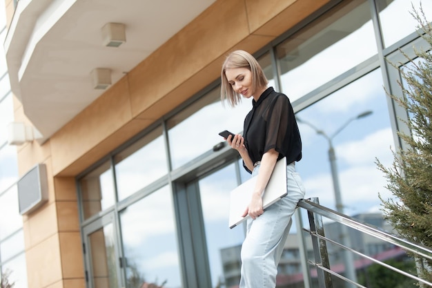 Femme d'affaires moderne parlant au téléphone et tenant un ordinateur portable dans les escaliers à l'extérieur