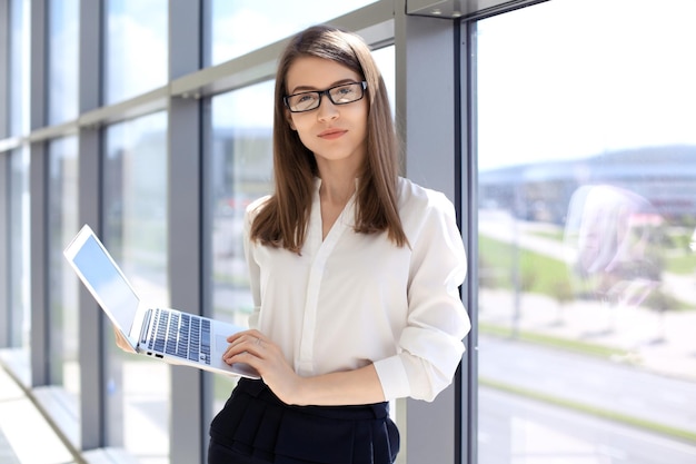 Femme d'affaires moderne tapant sur un ordinateur portable tout en se tenant au bureau avant une réunion ou une présentation