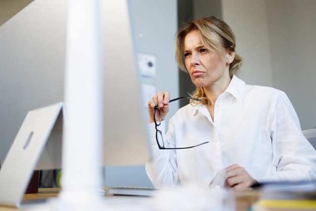 Une femme d'affaires mûre et pensive avec une expression inquiète travaille sur un ordinateur au bureau