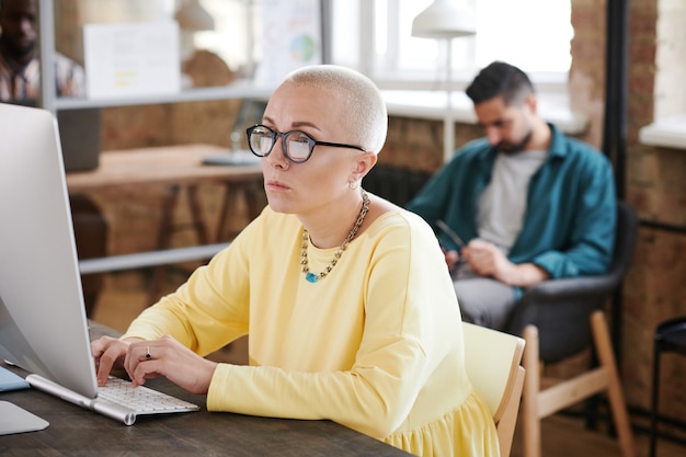 Femme d'affaires mûre sérieuse dans des lunettes se concentrant sur son travail en ligne à la table au bureau