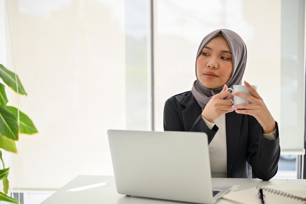 Femme d'affaires musulmane asiatique confiante en sirotant un café du matin en rêvant de succès