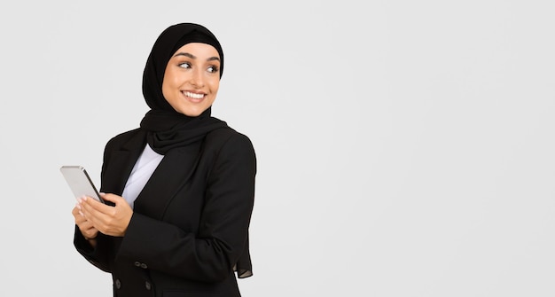 Une femme d'affaires musulmane en hijab souriant avec son smartphone en regardant l'espace libre
