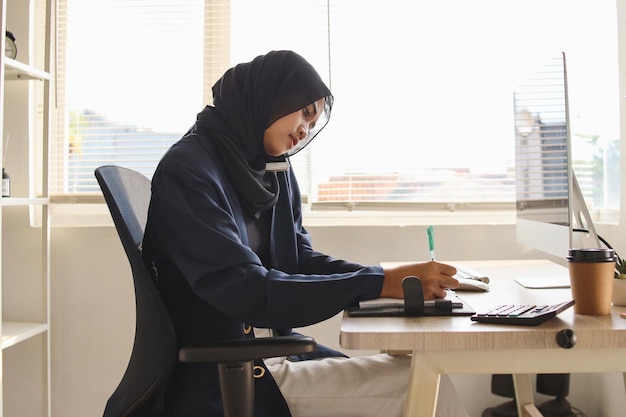 Femme d'affaires musulmane travaillant avec ses papiers tout en ayant une conversation d'affaires sur un téléphone portable.