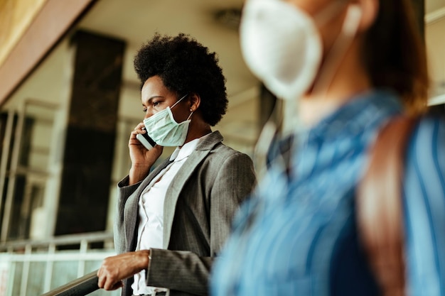 Femme d'affaires noire portant un masque facial comme protection contre les virus et parlant sur un téléphone portable en marchant au terminal de l'aéroport