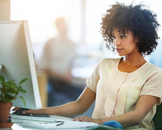 Femme d'affaires noire sérieuse et réfléchie travaillant sur un ordinateur et faisant attention dans son bureau