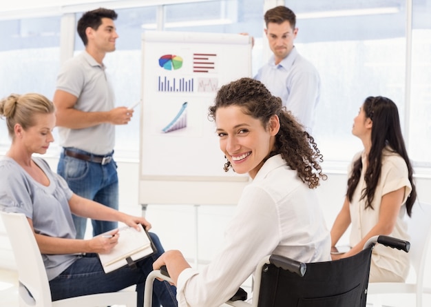 Femme d&#39;affaires occasionnel en fauteuil roulant, souriant à la caméra pendant la réunion